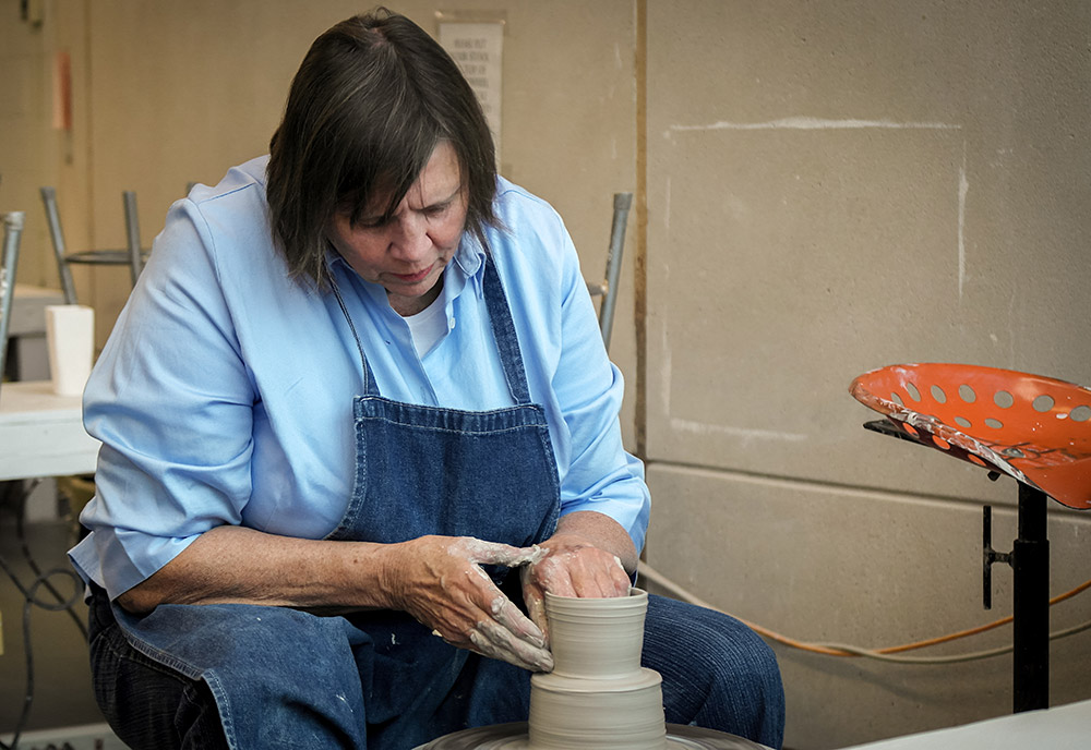 Woman sits working clay on a potter's wheel