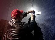 A man captures a pencil rubbing of a Servicemember's name engraved on the Vietnam Wall