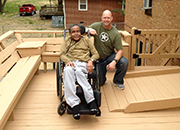 A Veteran in a wheelchair poses next to an accessible ramp to his house