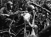 black and white photo showing three combat soldiers crouching in aforest
