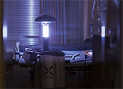 A tall, cylindrical machine stands in the center of a hospital room and emits blue light 
