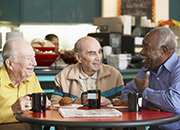 Elderly men, sitting at a table enjoying a cup of coffee while talking to one another