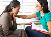 A woman with a sad expression is comforted by a therapist with her hand on the woman's shoulder