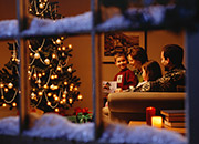 Looking through a wintery window at a family gathered around a Christmas tree.