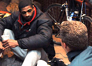 A man talks to a homeless man sitting by a brick wall