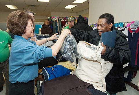 a woman hands a homeless man new clothes