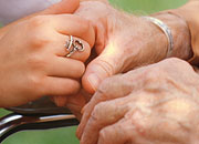 Hands of a caregiver holding hands of a man in a wheelchair