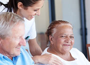 A smiling elderly man and woman are attended by a smiling nurse