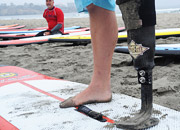 A man with a prosthetic leg stands on a surfboard in the sand