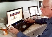 A man sitting at a computer holding a bottle of prescription medicine