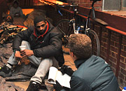 A man with a notepad talks with a homeless man at night on the street
