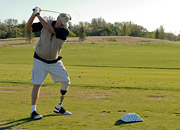 A man with a prosthetic leg swings a golf club at a driving range