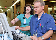 A man and woman nurse look at a computer and smile in a hospital corridor