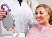 Woman looks at her smile in a mirror being held by a dentist