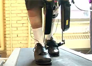 a researcher watches a woman walking on a treadmill attached to a robotic device