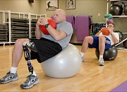 A man with a prosthetic leg and his son work out on exercise balls