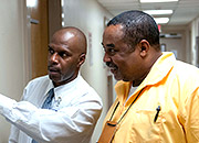 Two men talk and point to a bulletin board in a facility hallway