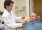 A dentist holds up a mold of a face next to his patient