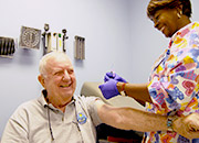 A nurse applies a bandaid to the shoulder of a smiling Veteran