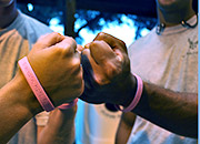 Two men wearing pink bracelets bump fists