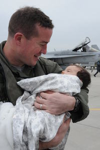 active duty male in front of fighter jet holding a baby