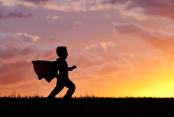 little boy in a cape running on a hill with a beautiful sunset in the background