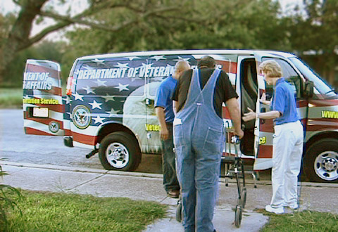Volunteers help a veteran into a VA van