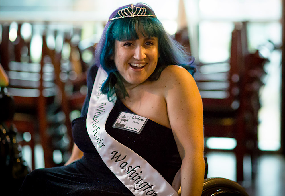 A woman with a crown in a wheelchair smiles 