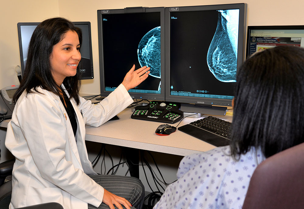 A woman in a lab coat shows a patient two computer monitors displaying mammogram images