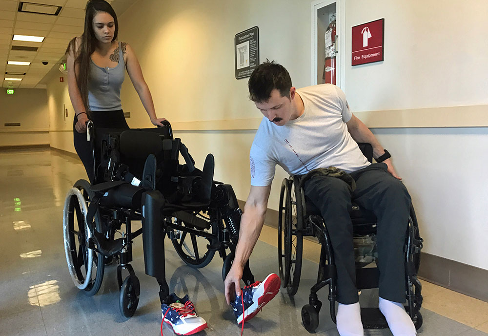 Veteran Brandon Myers removes his shoes from a wheelchair he used to harness an exoskeleton walking device