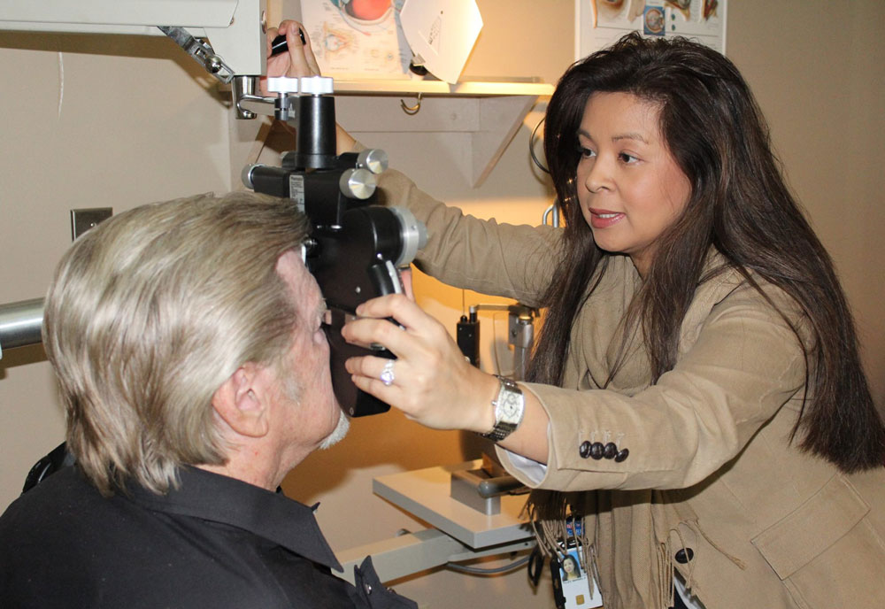 Female doctor performing an eye exam on a male Veteran patient.