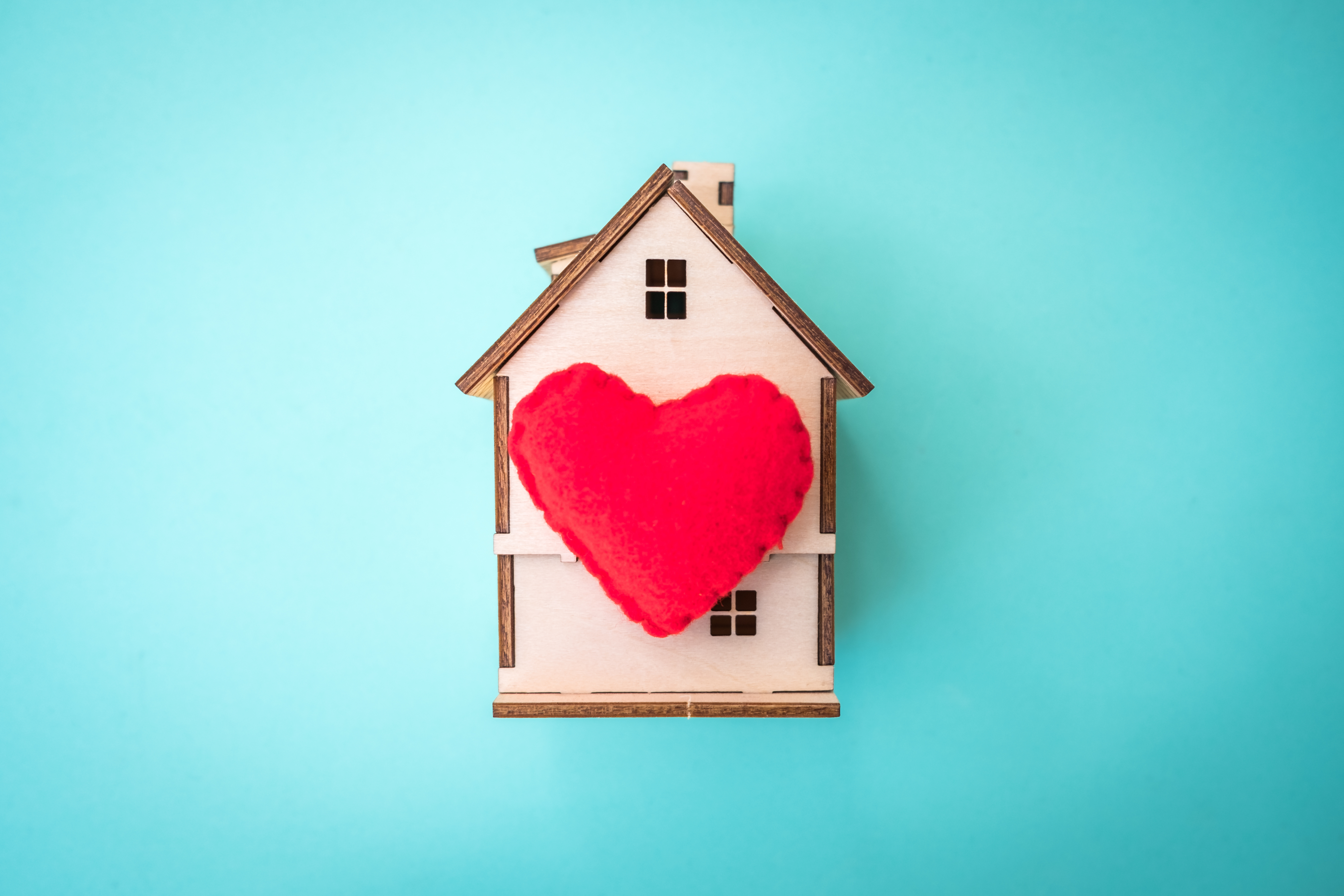 a granite teal background with a tan, wooden model of a house with a read heart in the middle. 