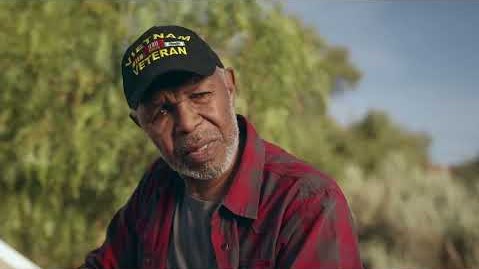 An older African American male outside wearing a Vietnam Veteran hat looking toward the camera slighAn older African American male outside wearing a Vietnam Veteran hat looking toward the camera slightly to the right.