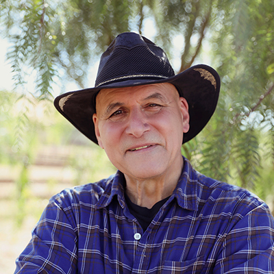 A old man in a cowboy hat smiling at the camera.