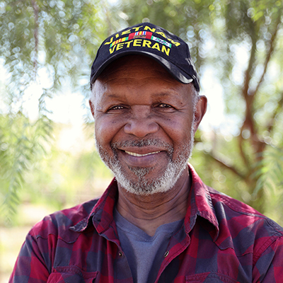 A old man in a Vietnam Veteran baseball hat smiling at the camera.