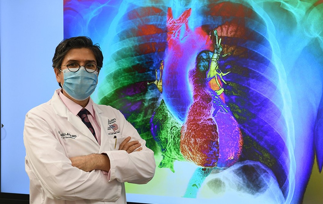 A physician standing next to a colorful x-ray displaying ribs, lung and heart.