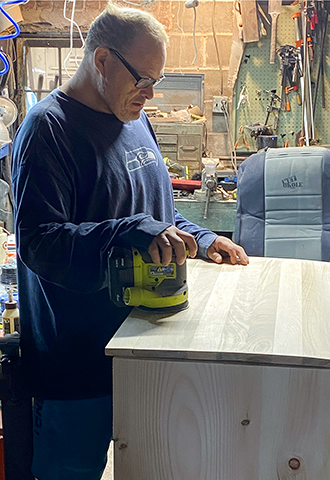 A man standing in a workshop sanding a butcher block table.