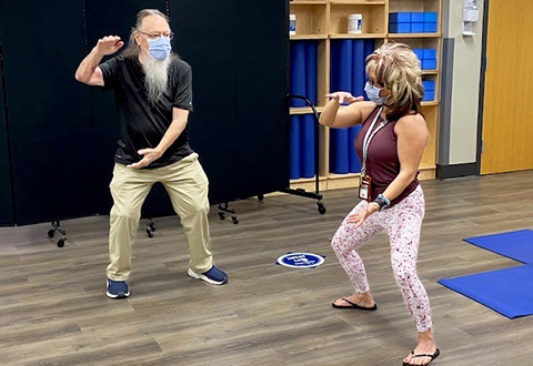 older man practicing tai chi with female instructor wearing masks