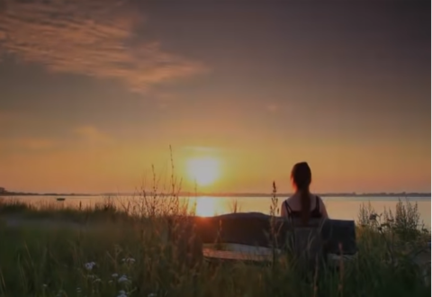 Woman sitting on bench looking at sunset