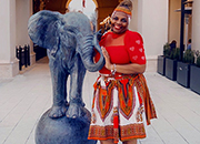 Air Force Veteran Karen Williams smiles and poses playfully in a red dress next to an elephant statue in front of an indoor restaurant.