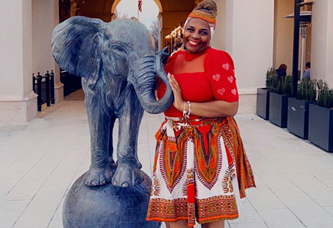 Air Force Veteran Karen Williams smiles and poses playfully in a red dress next to an elephant statue in front of an indoor restaurant.