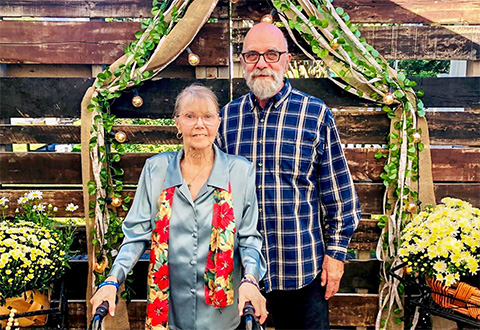 Older woman and man in front of wood panels and arch decorated with green and gold 