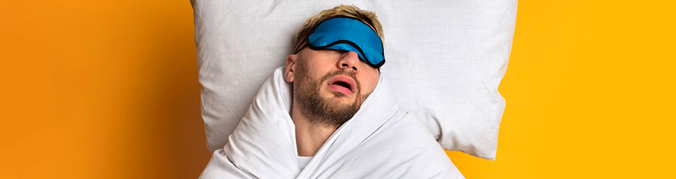 man sleeping while wrapped in blankets and wearing a sleep mask