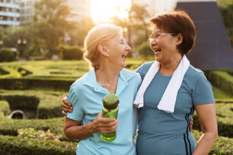 Two women laughing outside. One woman is holding a water bottle, the other has a towel around her neck