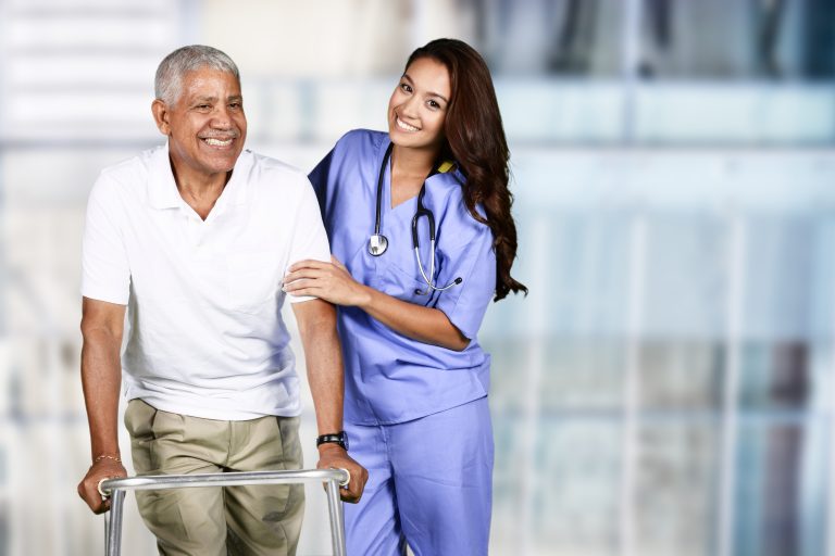 Young woman nurse in blue scrubs walking with an older patient using a walker