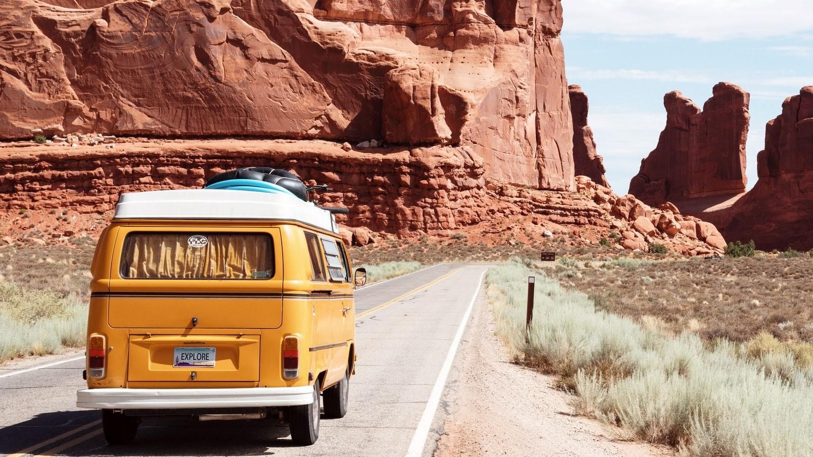 A VW van driving a highway though a steep cliffed desert setting.