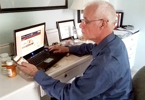 A man sitting at a computer holding a bottle of prescription medicine.