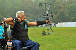 Using a compound bow, a male athlete pulls back on the arrow and aims at the target.