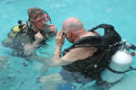 A man in a pool wearing SCUBA gear receives instructions from a female instructor.