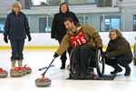 A man in a wheelchair prepares to slide a curling stone across the ice towards the house (target).